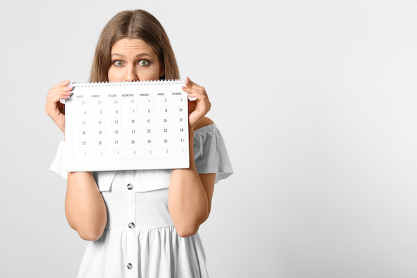 Young woman holding calendar with marked menstrual cycle days on light background. Space for text